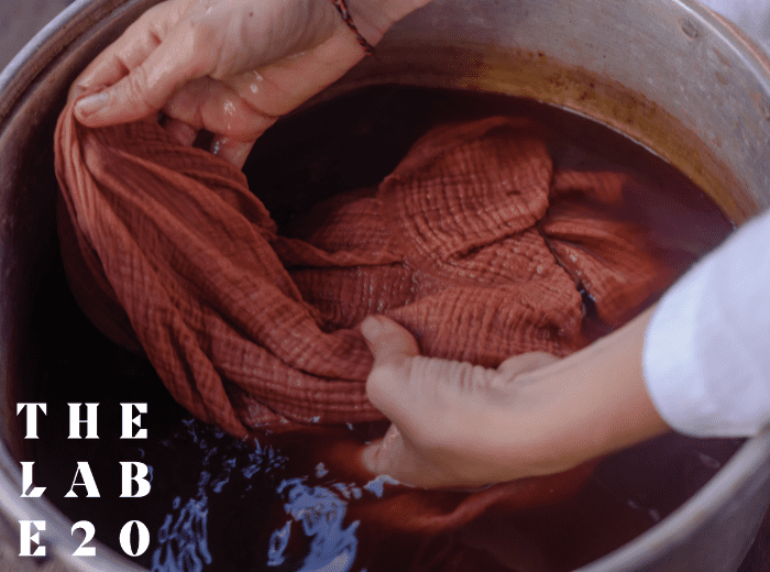 Hands dyeing a garment in a bucket with The Lab E20 logo overlayed