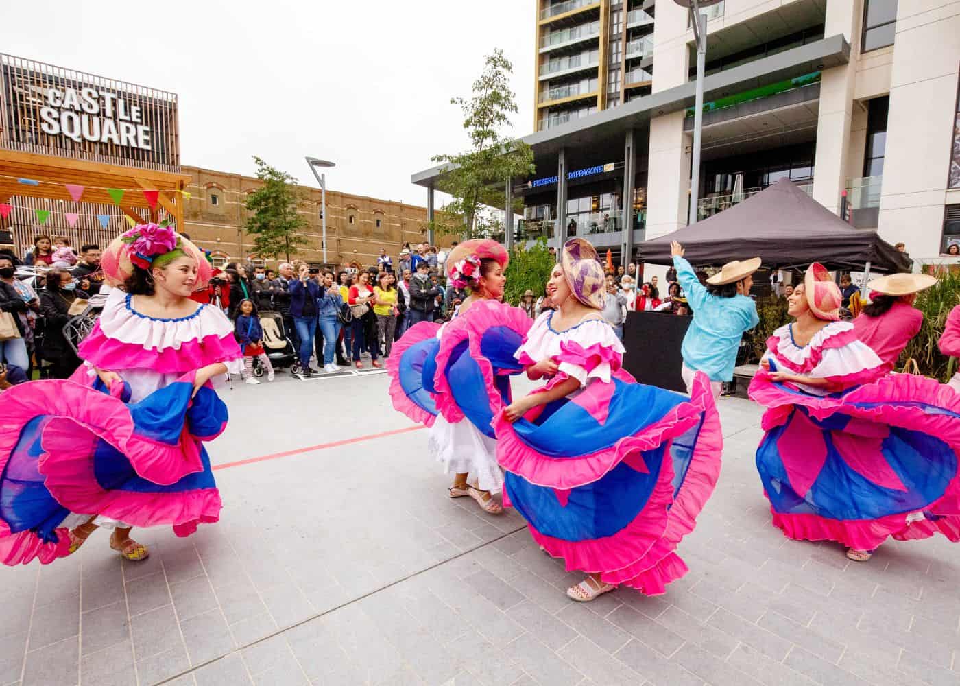 Women dancing in Castle Square wearing traditional Latin American dresses with a crowd watching
